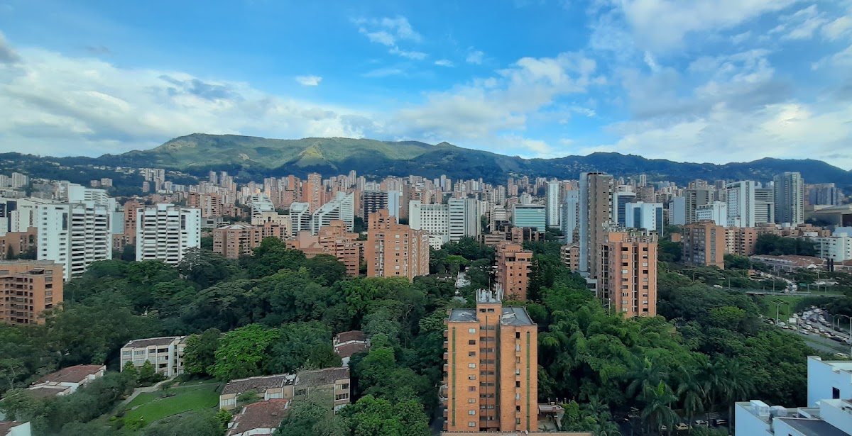 Panoramic view of El Poblado, Medellín with modern high-rise buildings, lush green trees, and mountains in the background